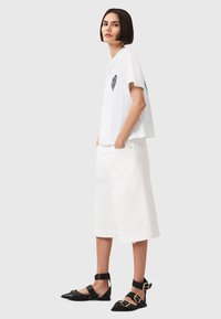 Hvid bomulds t-shirt med et sort hjerte grafik, parret med knælange hvide denimshorts. Sorte flade sko med ankelremme og guld accenter.