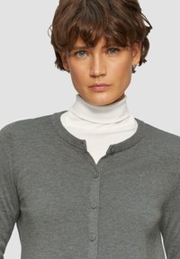 Grijze cardigan met een ronde halslijn, knoopdetails, gemaakt van een glad gebreid materiaal; gelaagd over een witte coltrui.