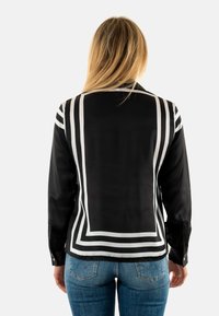 Camisa negra con patrones de rayas blancas en la parte posterior, mangas largas con cierres de botón y tela elegante con una textura suave.