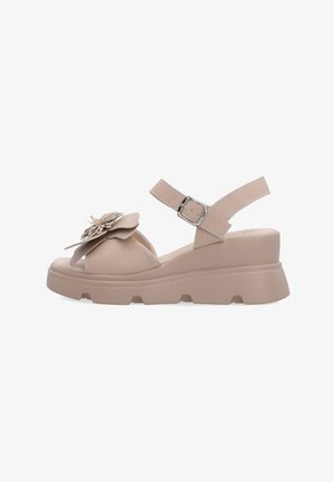 Beige kilesandal med tyk sål, rem med spænde om anklen og stor dekorativ blomst på frontremmen.