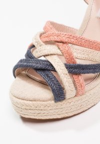 Sandale à plateforme avec des brides tissées en rose, beige et marine. La tige est en tissu texturé avec une semelle en jute.