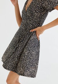 Robe à manches courtes à fleurs en marine avec de petites fleurs blanches et beiges, décolleté en V, taille cintrée et poches latérales, fabriquée en tissu léger.