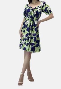 Kortärmad klänning i ljusgrön med blommönster i mörkblått och vitt. Har en smockad bodice och en knytdetalj vid halsringningen.