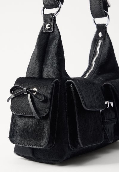 Sort håndtaske lavet af tekstureret kunstpels, med to frontlommer med sløjfer, sølvhardware og lynlås lukning øverst.