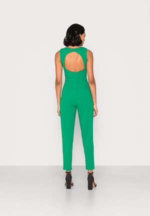 Macacão verde com um design ajustado, corte sem mangas e costas em forma de chave. Apresenta um fecho oculto e pernas ajustadas, combinado com saltos pretos.