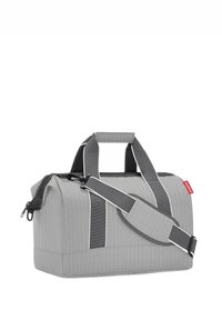 Grauem Duffle-Bag mit vertikaler Rippstruktur, kontrastierenden weißen Akzenten, oberen Tragegriffen und einem verstellbaren Schultergurt. Mit Reißverschluss.