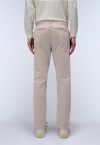 Pantaloni in cotone beige con gambe dritte, tasche posteriori, cuciture pulite e una texture liscia. Indossati con sneaker di colore chiaro.