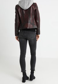 Burgunderfarbene Lederjacke mit grauem Kapuzenpulli, enganliegenden schwarzen Jeans und schwarzen Ankle Boots. Die Jacke hat ein asymmetrisches Design und silberne Hardware.