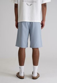 Light blue shorts with a relaxed fit, knee-length design, and smooth texture. Worn with a white shirt and brown slip-on shoes.