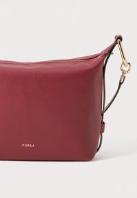 Borsa a tracolla in pelle bordeaux con texture liscia, finiture dorate e chiusura con zip. Caratterizzata da una tracolla removibile e logo impresso.