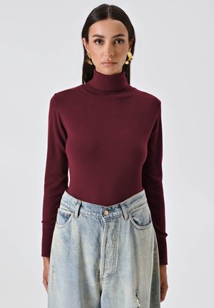 Body en col roulé bordeaux en tissu doux, associé à un jean en denim léger déchiré taille haute avec poches.