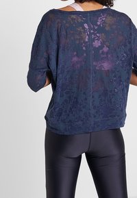 Tmavě modrý oversized top s květinovým vzorem, krátkými rukávy a volným střihem, doplněný černými legínami. Měkká, lehká látka.