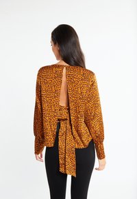 Leopardprint blouse in oranje en zwart, met lange mouwen, een uitsnede op de rug en een gestrikt hem gedeelte. Glad materiaal en een losse pasvorm.
