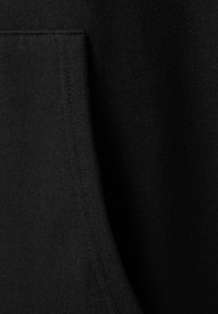 Zwarte stof dichtbij met een rechthoekige genaaide zak en zichtbare stiksels op een getextureerd materiaal.