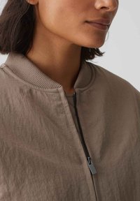 Giubbotto bomber color beige con finitura testurizzata, colletto a coste e zip nera. Caratterizzato da un tessuto leggero e sgualcito per un look rilassato.