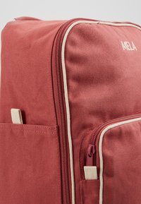 Sarkans auduma mugursoma ar krēmkrāsas akcentiem, ar rāvējslēdzēja kabatu un sānu kabatu. Materiāls ir ar teksturētu apdari.