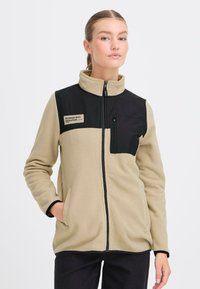 Fleecejack in beige met een zwart bovenpaneel. Voorzien van een ritszak, staande kraag en twee zijzakken. Gelaagde stof.