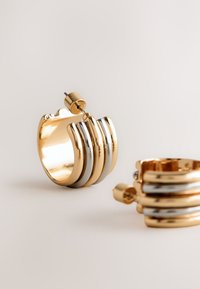 Gold and silver hoop earrings with three stacked bands, featuring a polished finish and a secure post-back closure.