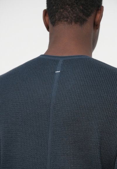 Dunkelblauer strukturierter Pullover mit Rundhalsausschnitt und einer sichtbaren Naht hinten, versehen mit einem kleinen weißen Akzent am Halsauschnitt.