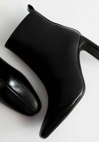 Zwarte leren enkelboots met puntige neuzen en hoge, slanke hakken, weergegeven vanuit zij- en bovenaanzichten op een witte achtergrond.