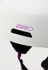 Bijela kaciga s ljubičastim logom i akcentima. Ima ventilacijski otvor i crnu bradu trak. Glatka površina, zaobljenog oblika, lagana konstrukcija.