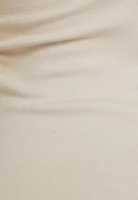 Béžová žebrovaná látka s jemnou strukturou a mírným pružením, vytvářející hladký povrch s jemnými vertikálními liniemi po celé ploše.