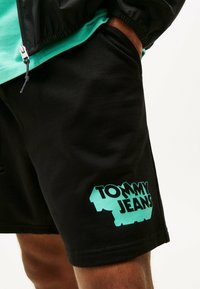 Zwarte shorts van een katoenmix, voorzien van een groot turquoise "TOMMY JEANS" logo op het linkerpijpzand. Soepele textuur, regular fit.