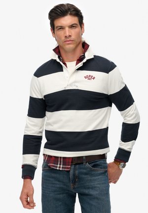 Marineblauw en witte gestreepte long-sleeve polo shirt, met een knoopsluiting en geborduurd "SUPER DRY" logo. Draagt over een rood geruit shirt.