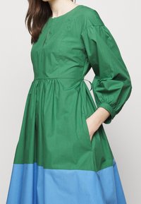Robe en coton bi-colore vert et bleu avec un col rond, des manches bouffantes, une taille froncée et des poches latérales.