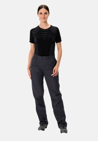 T-shirt noir à manches courtes évacuant l'humidité, avec des détails en mesh, associé à un pantalon léger gris foncé à taille élastique et des chaussures sombres.