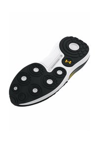 Semelle de chaussure de sport en noir et blanc avec des motifs de traction circulaires et un logo Under Armour jaune près du talon.