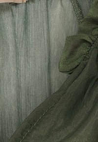 Gröna tyget har en mjuk textur och en lätt lyster. Materialet har subtila vertikala linjer och en rynkad detalj vid kanten.