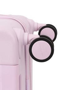 Gros plan de deux roues roses de valise avec bords noirs attachées à un coin de valise rigide rose clair.