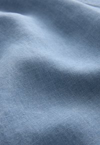 Tessuto azzurro chiaro con una trama liscia e un motivo di tessitura sottile, che mostra pieghe morbide e variazioni naturali di luce.