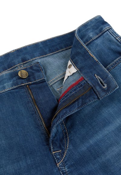 Blue denim jeans with partially unzipped zipper, visible button labeled "INCOTEX," and folded waistband showing white and red fabric detail.
