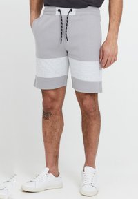 Shorts en coton gris clair avec un panneau texturé gris, taille élastique et cordon de serrage noir contrastant. Portés avec des baskets blanches.