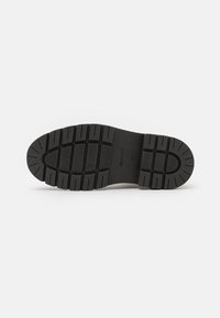 Semelle noire en caoutchouc avec motif antidérapant texturé, comprenant des crampons profonds et une finition lisse. Nom de la marque gravé affiché sur la semelle.