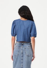 Blå denimkort topp med puffärmar, vita prickar och elastiska manschetter. Matchad med en högmidjad bleknad denimkjol.