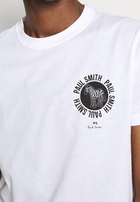 Weißes Baumwoll-T-Shirt mit einem kreisförmigen schwarzen Grafik eines Zebras, darunter der Text "Paul Smith" und die Unterschrift. Klassischer Rundhalsausschnitt.