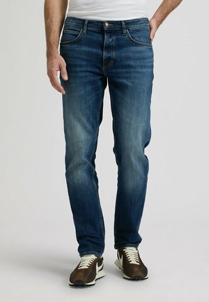 Ciemnoniebieskie dżinsy z denimu z efektem sprania, o prostych nogawkach, z pięcioma kieszeniami i klasycznym zapięciem na guzik. Połączone z brązowo-białymi trampkami.