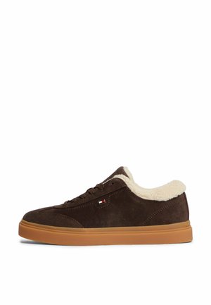 Ciemnobrązowy zamszowy sneaker z jasnobrązową podeszwą i białą podszewką z polaru widoczną wokół kołnierza przy kostce, z bocznym detalem logo.