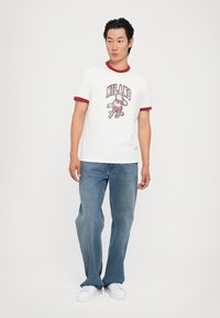 Hvid bomulds t-shirt med rød ribbet krave, der har "MILANO" grafik. Båret med lyseblå denim jeans og hvide sneakers.