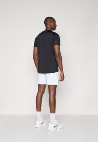 Chemise noire à manches courtes au design épuré, accompagnée d'un short blanc. Les chaussures sont blanches avec des accents noirs. Texture lisse, style décontracté.