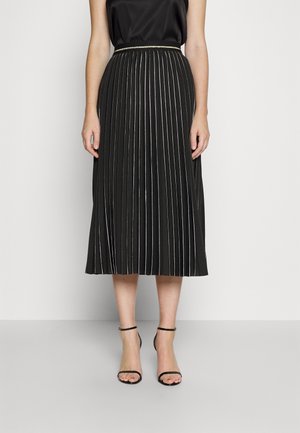 Femme portant un haut noir sans manches, une jupe midi plissée noire avec de fines rayures blanches, et des sandales à talons altos avec bride à la cheville noires.