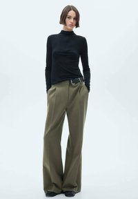 Black long-sleeve top with a high neckline, paired with olive wide-leg trousers and a black belt. Smooth texture, structured silhouette.