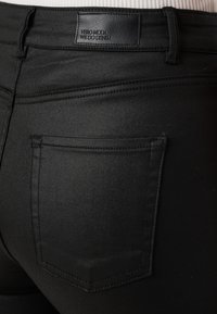 Svarta denimjeans med en slät textur och en figursydd design. Har en bakficka och en läderetikett med texten "VERO MODA WE DO DENIM".