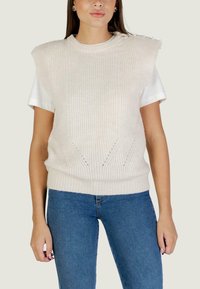 Maglione a collo rotondo in beige chiaro, caratterizzato da una texture a coste, dettagli sulle spalle e inserti a rete. Indossato sopra una T-shirt bianca.