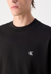 Maglietta in cotone nera con collo rotondo e maniche corte. Presenta un logo ricamato bianco all'angolo sinistro del petto. Texture morbida.