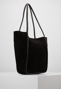 Svart mocka toteväska med släta läderdetaljer, två långa remmar, en mjuk textur och en strukturerad form. Minimalistisk design.