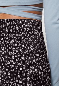 Czarna spódnica plisowana z małym białym wzorem kwiatowym, połączona z jasnoniebieską bluzką z długim rękawem z materiałem skrzyżowanym w talii.